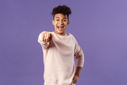 Portrait of outgoing happy hispanic male student making his choice, laughing over something extremely funny point finger at camera with amused smile, standing purple background.