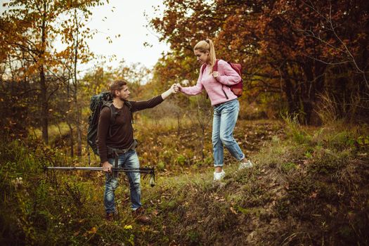Intelligent tourist supports his woman on a hill descent. A man holds a woman's hand while supporting her on a difficult walking route. Hiking concept.