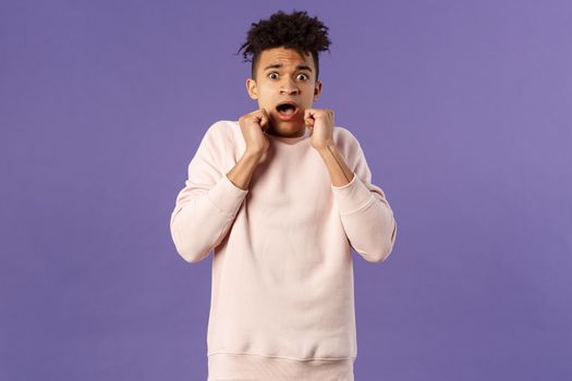 Portrait of scared hispanic guy screaming from fright, hold hands near face, open mouth gasping express fear and terrified emotion from watching horror movie, terrible accident, purple background.