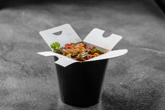 Wok in box rice noodles in black food container. Fast food delivery service. Takeaway chinese street meal