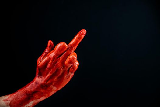 Female hand stained with blood shows the middle finger on a black background