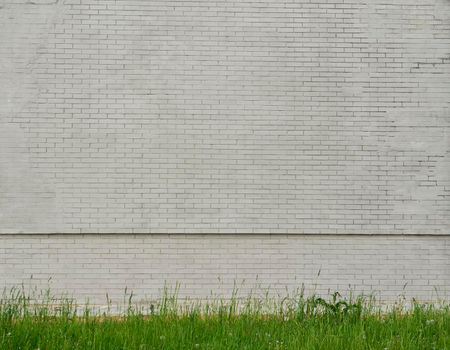 Old shabby gray brick wall of a building with green grass underneath. Brick wall and grass background.