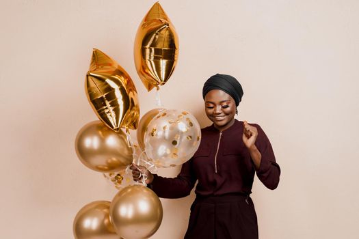 Muslim new year party with golden balloons for black woman. African attractive girl celebration of the end of year. Happy emotion