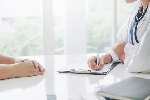 Woman doctor talks to female patient while writing on the patient health record in hospital office. Healthcare and medical service.