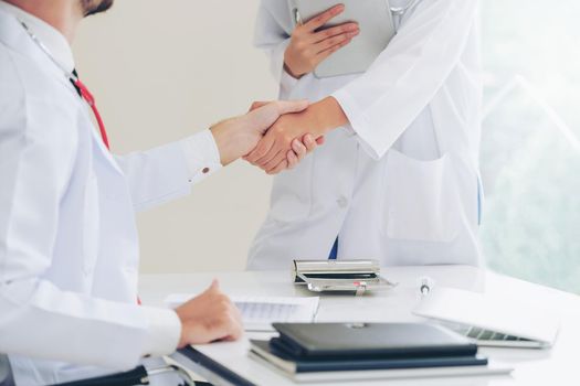 Doctor at the hospital giving handshake to another doctor showing success and teamwork of professional healthcare staff.