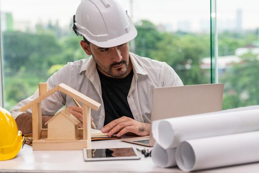 Young man architect or engineer working at desk with designer equipment to make interior design at workplace. Real estate business and civil engineering concept.
