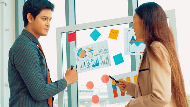 Business people work on project planning board in office and having conversation with coworker friend to analyze project development . They use sticky notes posted on glass wall to make it organized .