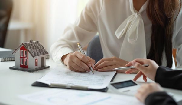 Close up woman signs contract behind home architectural model.