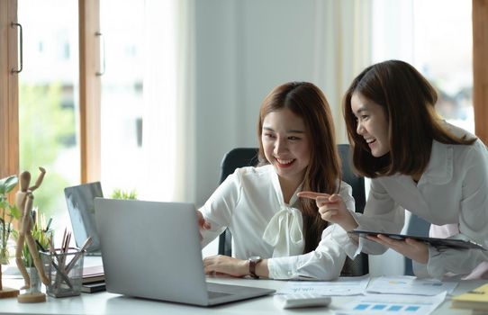 Two young beautiful asian business woman in the conversation, exchanging ideas at work..