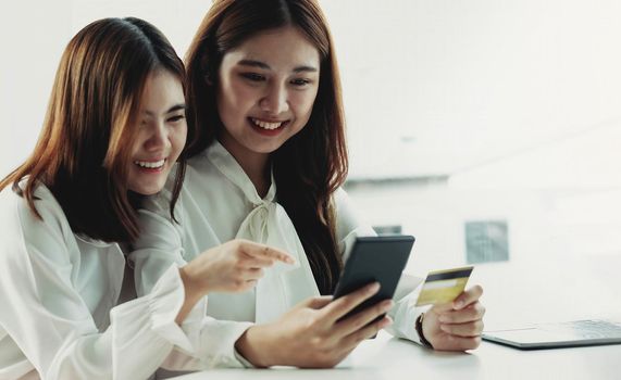 Two young Asian women hold credit cards and happily use their mobile phones for online shopping. business concept and technology digital marketing casual lifestyle