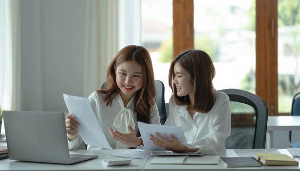 Two young beautiful asian business woman in the conversation, exchanging ideas at work..