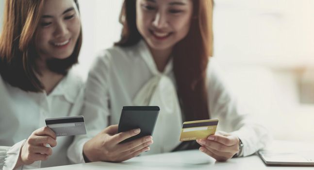 Two young Asian women hold credit cards and happily use their mobile phones for online shopping. business concept and technology digital marketing casual lifestyle