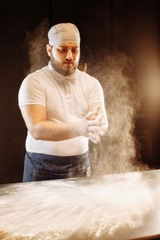 Making dough by hands at bakery or at home. Flour cloud in the air.