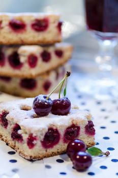 A slice of cherry pie on a linen napkin with polka dots. A cake decorated with fresh cherries. Next to a glass of juice. From the series "Homemade Cherry Pie"