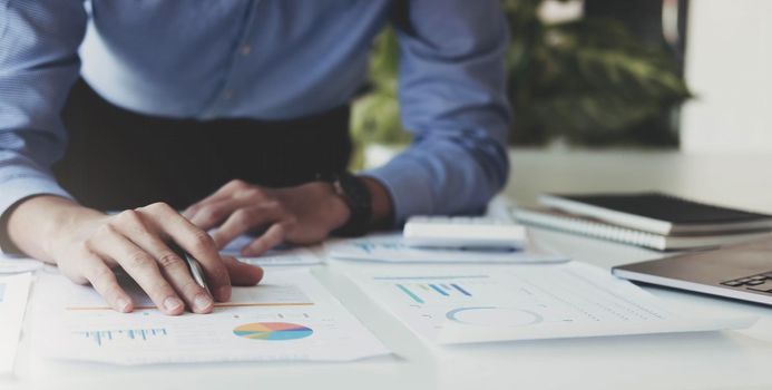 Close up Businessman hand holding pen and pointing at financial paperwork, financial charts to analyze profit concept.