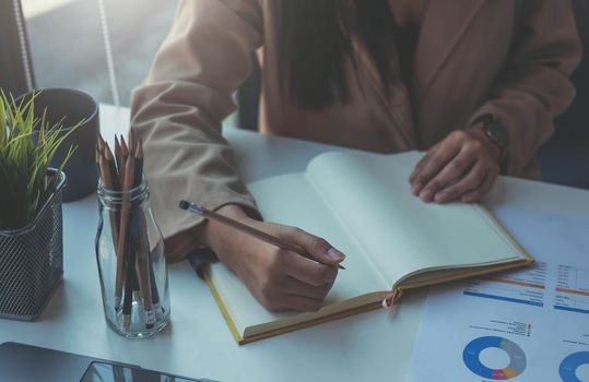 Closeup image of a woman writing and taking note on notebook in office, accounting financial concept.