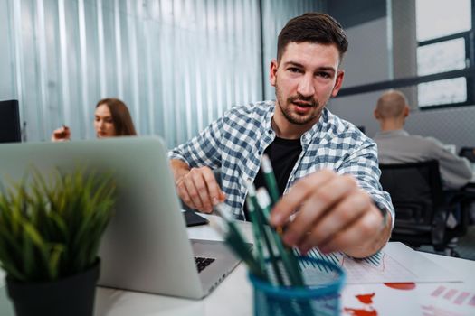 Portrait of young man sitting and working at his desk in the office, close up