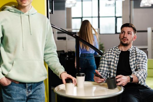 Two male colleagues having a talk while coffee break in office, close up