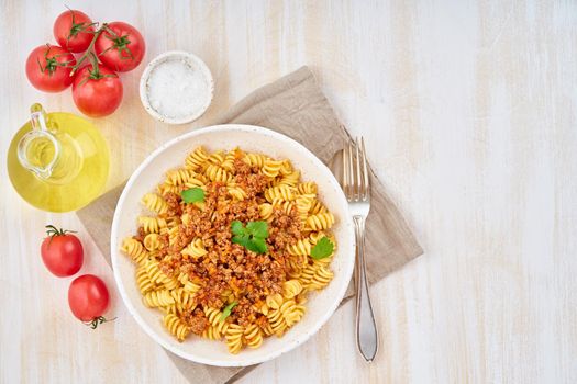 Bolognese pasta. Fusilli with tomato sauce, ground minced beef. Traditional italian cuisine. White wooden table. Top view, copy space