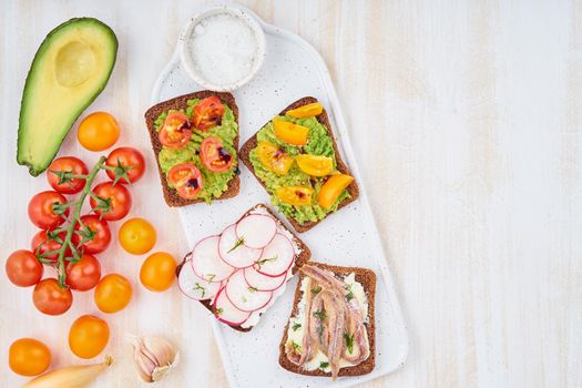 Set of smorrebrods with fish, anchovies, avocado, tomatoes, radish. Top view, copy space, white background.