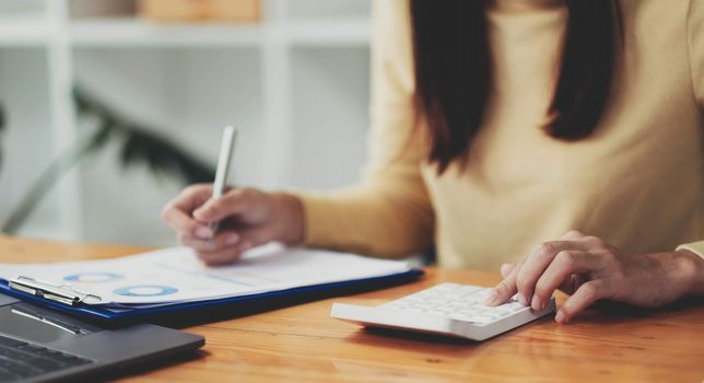 Close up Businesswoman using calculator and laptop for calaulating finance, tax, accounting, statistics and analytic research concept.