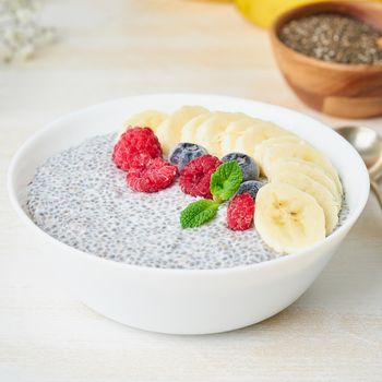 Close up Chia pudding in bowl with fresh berries raspberries, blueberries. Side view, white wooden light background.