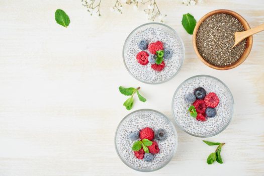 Chia pudding, top view, copy space, fresh berries raspberries, blueberries. Three glass, light wooden background, flowers, close up