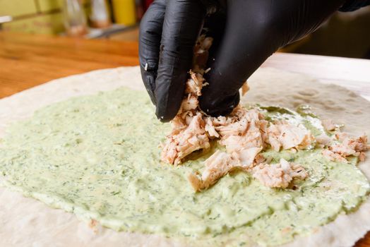 Burrito cooking process. Cook adds meat to pita with sauce. The process of making burrito. Mexican dish.