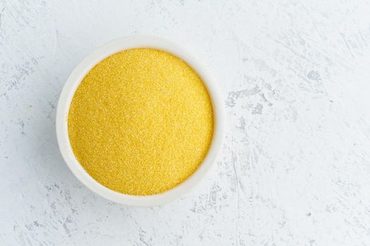 Corn, polenta in a white bowl on white background. Dried cereals in cup, vegan food, fodmap diet. Top view, close up.