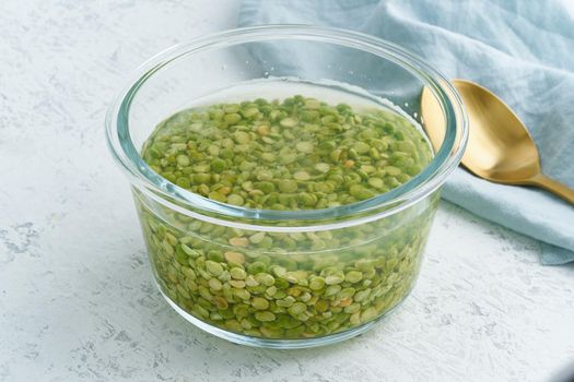 Soaking green peas cereal in a water to ferment cereals and neutralize phytic acid. Large glass bowl with grains flooded with water. Side view, close up, white background