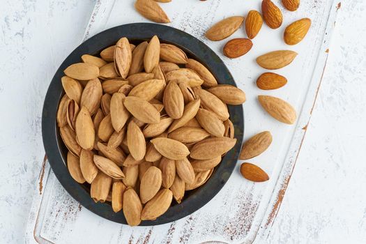 Top view plate with almonds in endocarp, bowl with drupe in shell on a white wooden cutting board. White background, overhead, copy space, close up