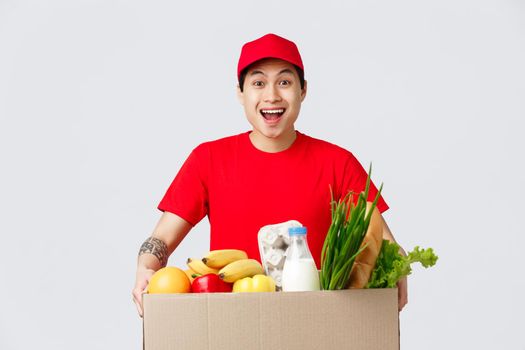 Online shopping, food delivery and internet stores concept. Friendly smiling asian courier in red cap and t-shirt, holding package with groceries, fresh products for customer made order.