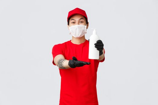 Delivery service worker giving client hand sanitizer. Cheerful courier hold sanitizer, wear medical mask and protective gloves during covid-19 self-quarantine, deliver orders in pandemic.