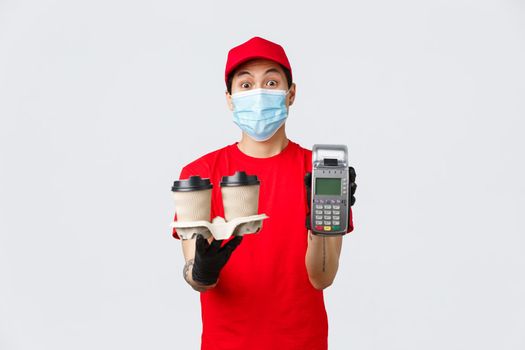 Contactless delivery, safe purchase and shopping during coronavirus concept. Asian courier or fast food employee showing POS terminal and coffee, paying terminal to customer, grey background.