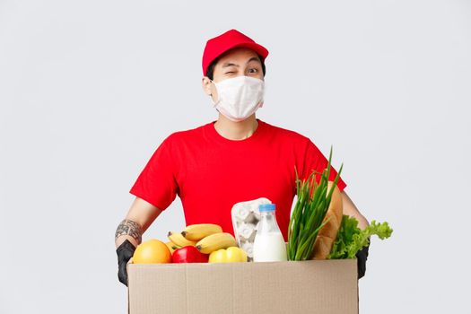 Online shopping, food delivery and coronavirus pandemic concept. Cheerful asian delivery guy bring customer online shop order, courier holding package with fresh groceries, employee deliver products.