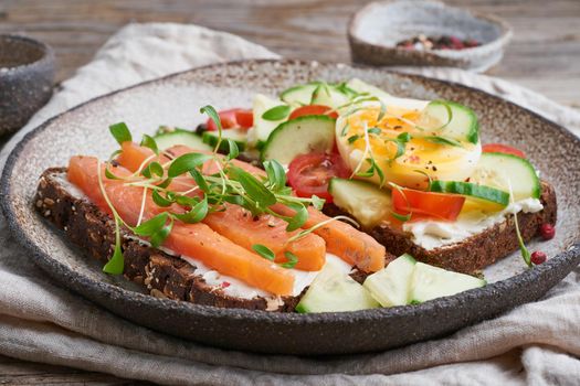 Smorrebrod - traditional Danish sandwiches. Black rye bread with a salmon, cream cheese, cucumber, tomatoes on a wooden table, side view.