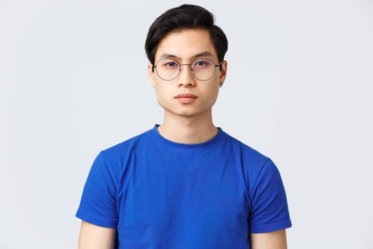 Lifestyle, people emotions and beauty concept. Close-up of serious-looking young hipster asian guy in glasses with nice fresh haircut, standing grey background with determined, confident expression.