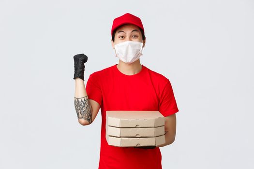Cheerful delivery guy fist pump, celebrating as deliver pizza to client house and got huge tips for courier service. achieve success, smiling pleased, wear medical mask and gloves.