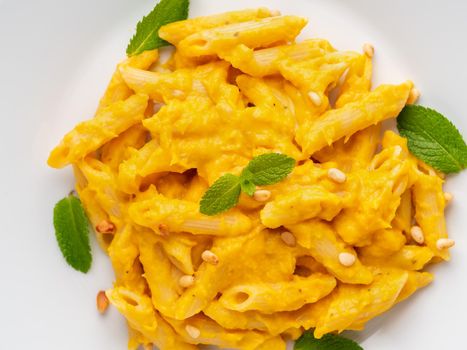 Pumpkin pasta penne with thick creamy sauce on white plate, top view, close-up