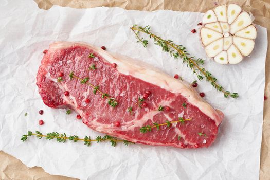 Big whole piece of raw beef meat, striploin on white parchment paper on craft background, zero waste packing. Seasoning steak with salt, top view, close up
