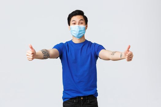 Different emotions, social distancing, self-quarantine on covid-19 and lifestyle concept. Friendly handsome asian guy in medical mask reaching hands for hug, embraces, or cuddles.