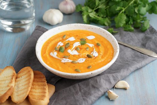 Pupmkin cream soup puree, dietary vegetarian lunch on blue wooden table, side view. Glass of water, toast, parsley, garlic.