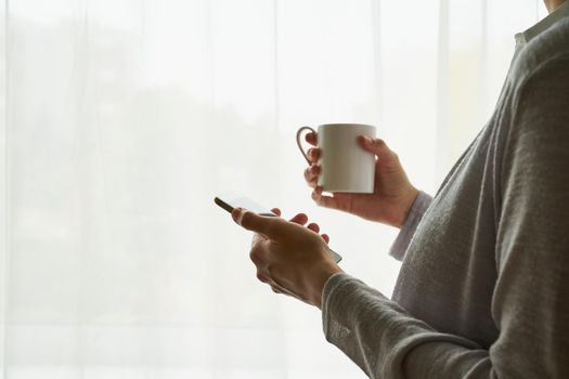 woman holding a cup of tea/coffee and using phone