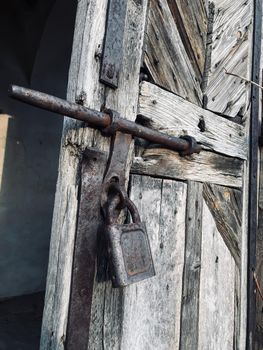 An old metal large rusty padlock is hanging on the old wooden gray plank doors.