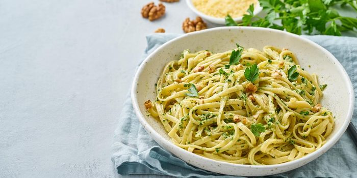 Banner with pesto pasta, bavette with walnuts, parsley, garlic, nuts, olive oil. Side view, long side, copy space, blue background