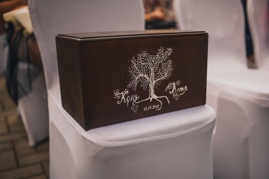 A brown box for gift envelopes painted with white paints with the names of the newlyweds. Drawn tree of life.