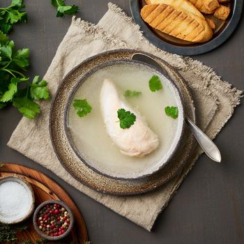 Chicken broth with chicken fillet, parsley and toast on dark brown background, top view