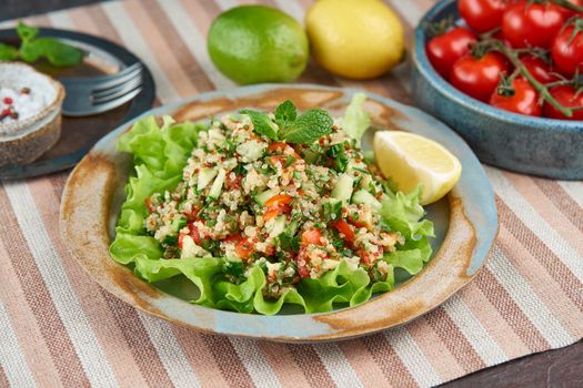 Tabbouleh salad with quinoa. Eastern food with vegetables mix, vegan diet. Side view, old plate