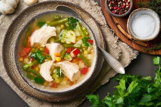 Homemade chicken soup with vegetables, broccoli on a dark brown background, top view