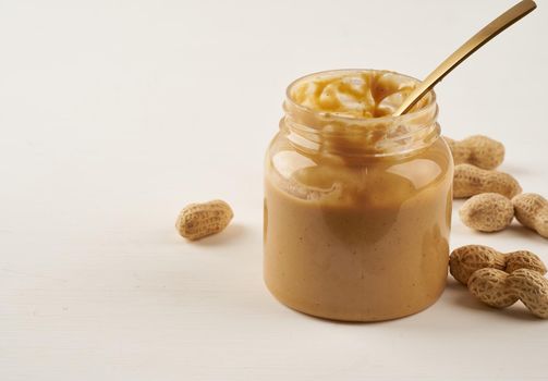 jar of peanut butter and peanuts in shell on a white table, side view, fresh ground crushed nuts, side view, copy space